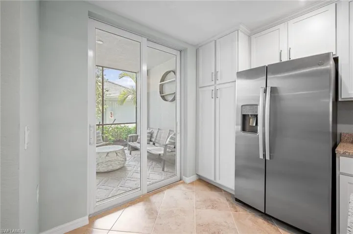 Kitchen with stainless steel fridge, white cabinetry, light tile patterned floors, and light stone countertops