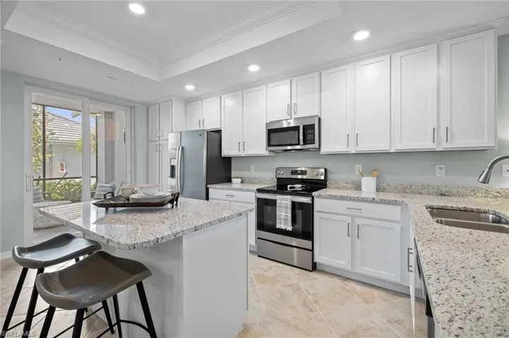 Kitchen featuring stainless steel appliances, ornamental molding, a raised ceiling, recessed lighting, and white cabinetry