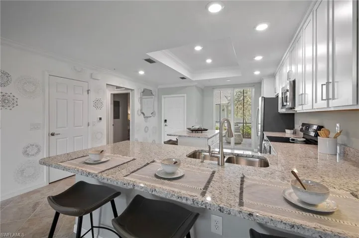 Kitchen with stainless steel appliances, ornamental molding, a kitchen breakfast bar, light stone countertops, and white cabinetry