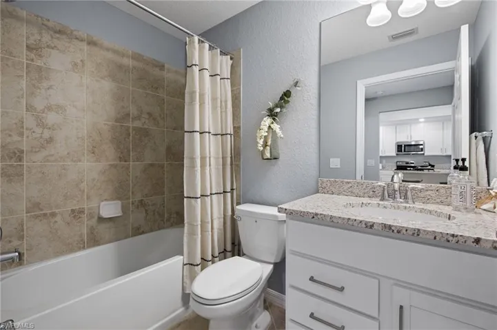 Full bathroom featuring a textured wall, vanity, and shower / bath combo with shower curtain