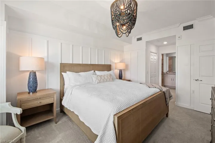 Bedroom with light carpet, a chandelier, ornamental molding, a decorative wall, and connected bathroom