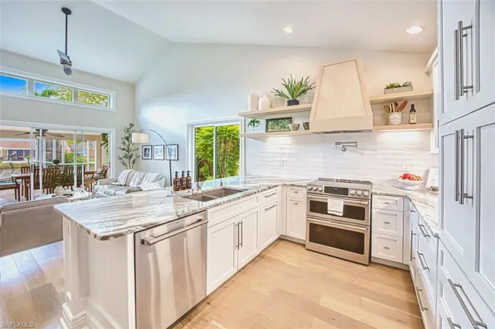 Kitchen featuring a peninsula, light stone counters, appliances with stainless steel finishes, light wood-type flooring, and premium range hood