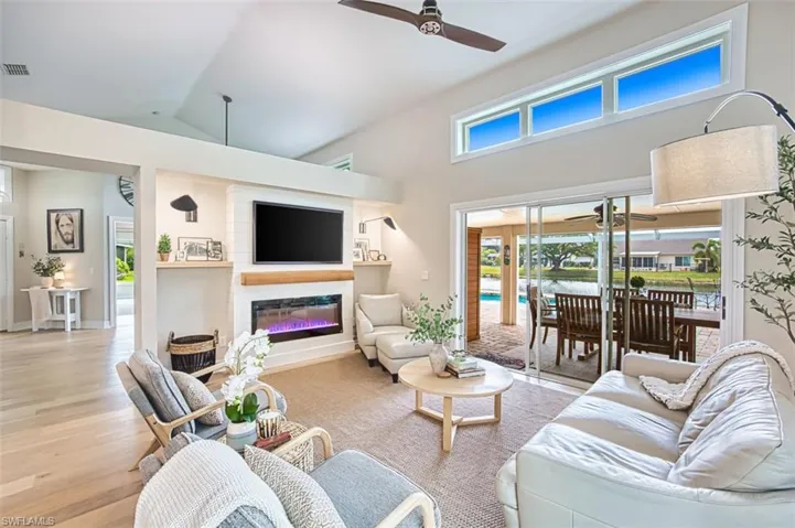 Living room with high vaulted ceiling, ceiling fan, light wood-style floors, a glass covered fireplace, and healthy amount of natural light