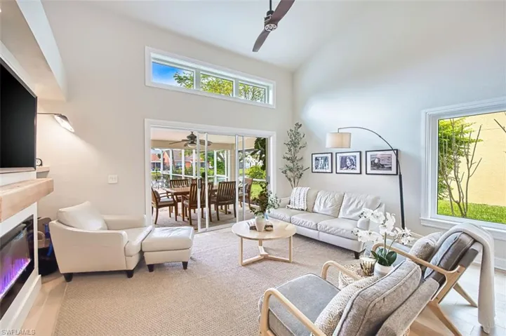 Living room with high vaulted ceiling, a ceiling fan, healthy amount of natural light, wood finished floors, and a glass covered fireplace