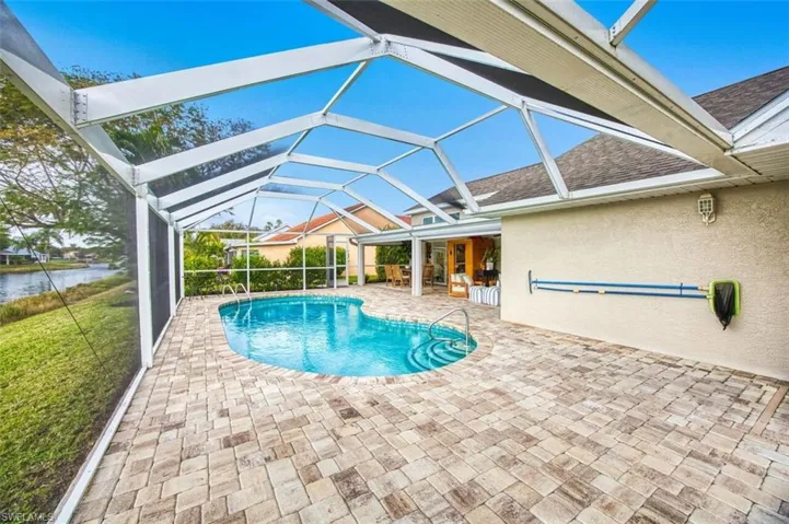 Swimming pool featuring glass enclosure, a patio area, a sunroom, and a water view