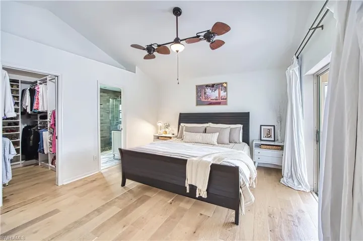 Bedroom featuring light wood-type flooring, lofted ceiling, a spacious closet, a ceiling fan, and ensuite bath