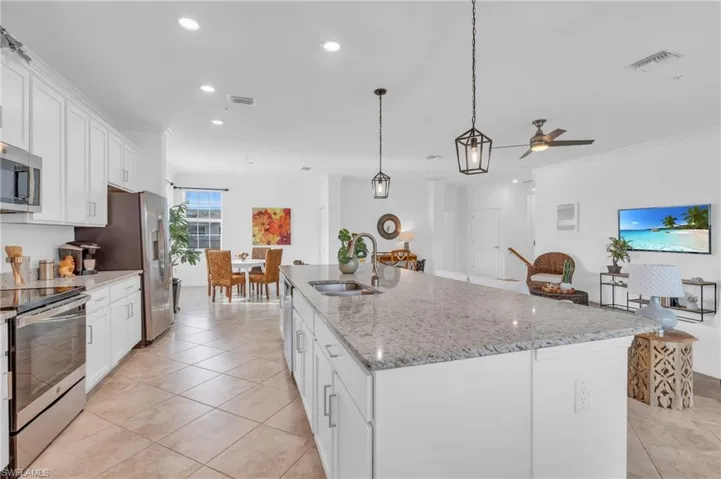 Kitchen with stainless steel appliances, a kitchen island with sink, decorative light fixtures, white cabinets, and sink