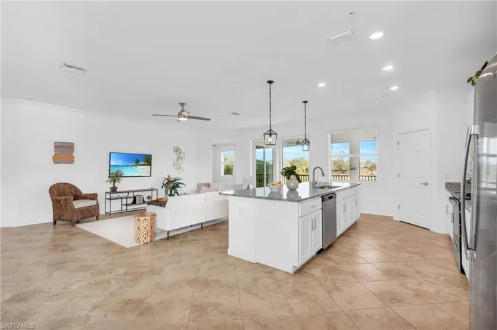 Kitchen with ceiling fan, dark stone countertops, stainless steel dishwasher, white cabinetry, and a kitchen island with sink