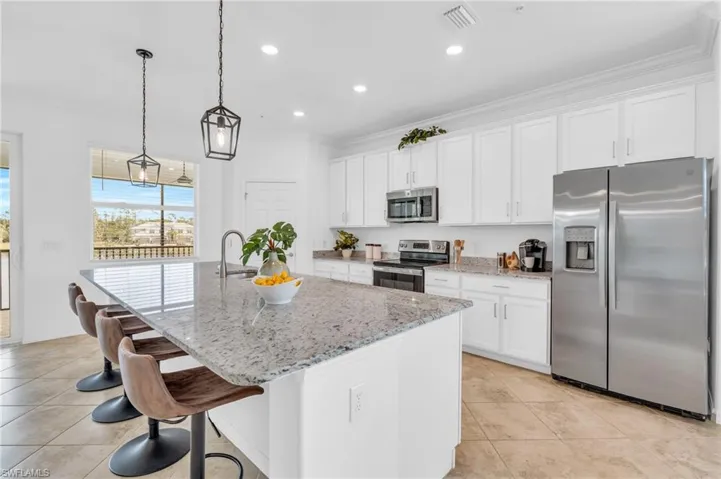 Kitchen with light stone countertops, pendant lighting, white cabinets, appliances with stainless steel finishes, and an island with sink
