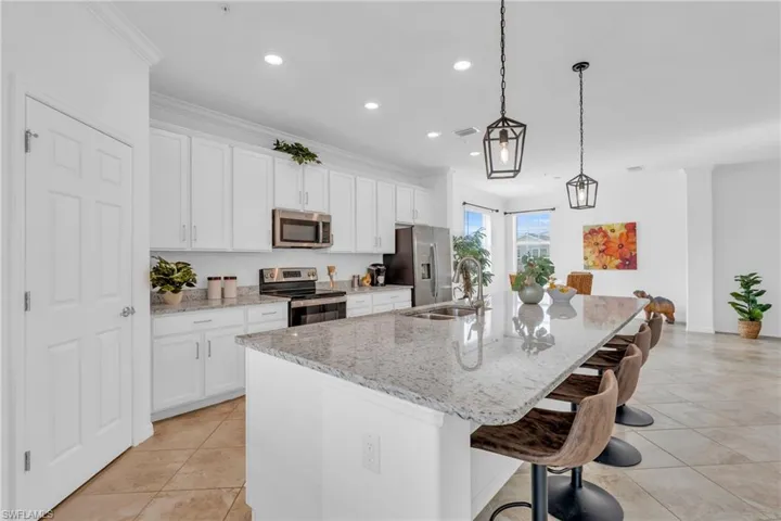 Kitchen with light stone countertops, decorative light fixtures, stainless steel appliances, an island with sink, and sink