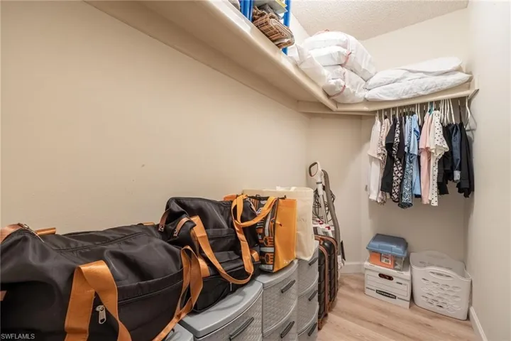 Neutral wall color, overhead shelving, clothes hanging rod, and wood-finish flooring