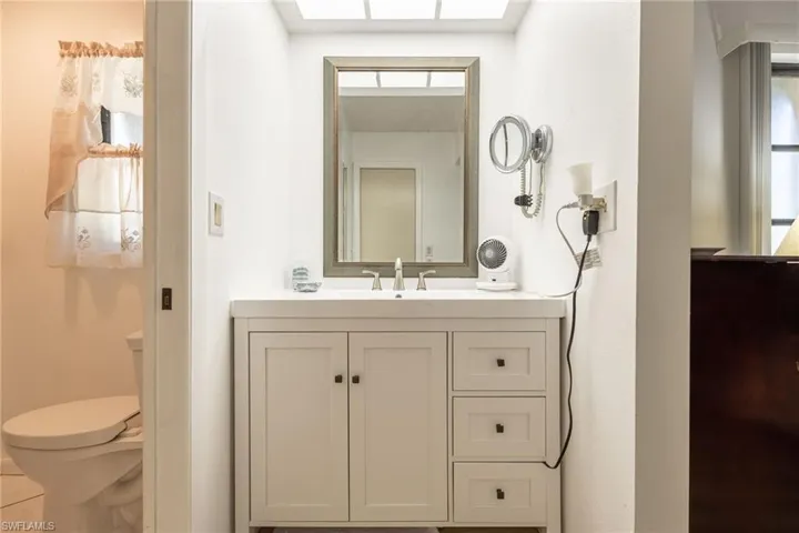 White vanity with shaker-style cabinetry, a built-in rectangular sink, and a framed mirror