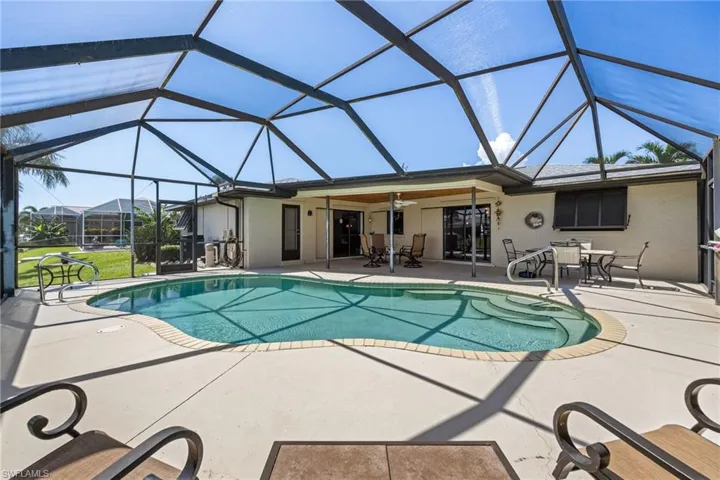 Screened pool enclosure with a freeform swimming pool, concrete patio, and covered patio area