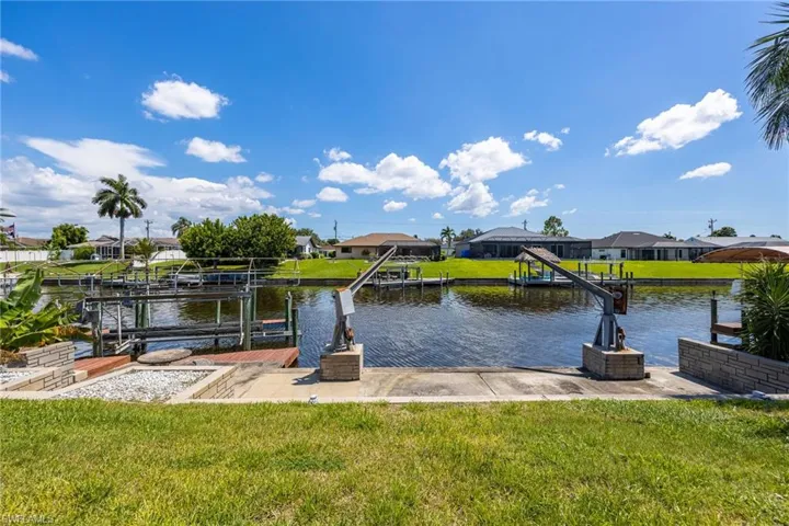 Waterfront property with boat lift, concrete boat ramp, and manicured lawn