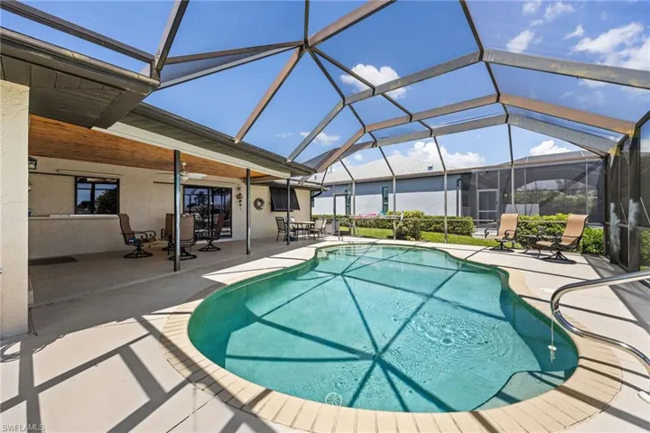 Screened enclosure with an in-ground swimming pool, concrete pool deck, and a covered patio featuring a wood-finish ceiling