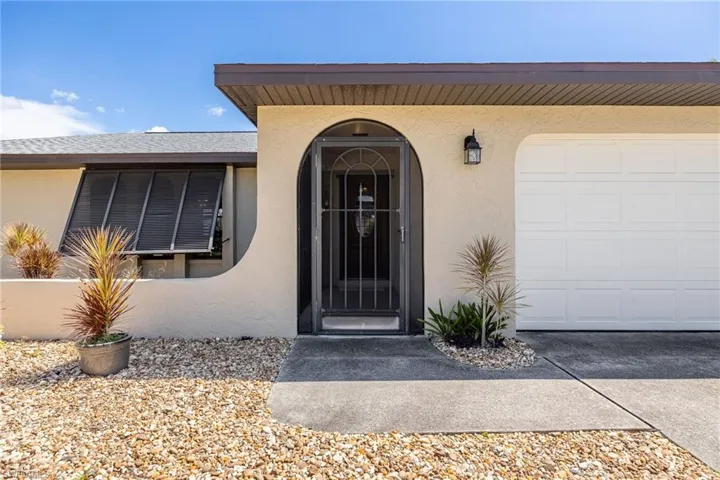Arched entry with security screen door, attached single-car garage, exterior wall lantern, and gravel landscaping