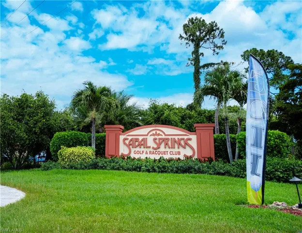 Entryway sign featuring "Sabal Springs Golf & Racquet Club" set against lush landscaping and mature palm trees
