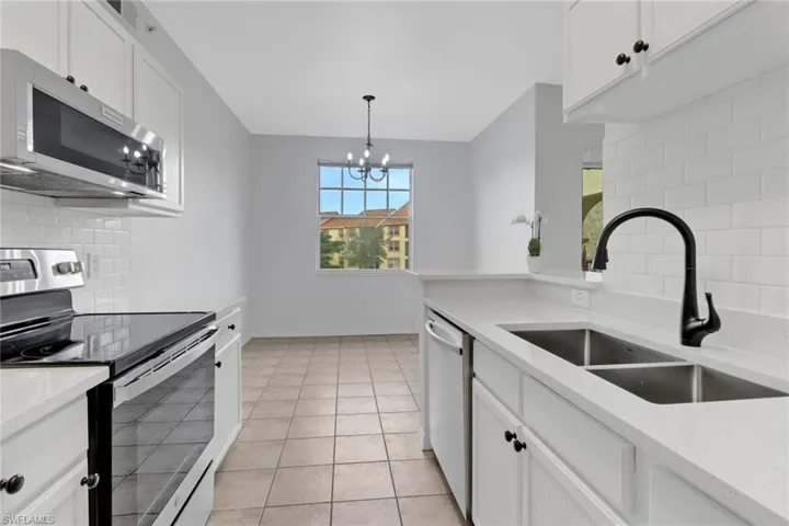 Kitchen with stainless steel appliances, a notable chandelier, sink, tasteful backsplash, and white cabinetry