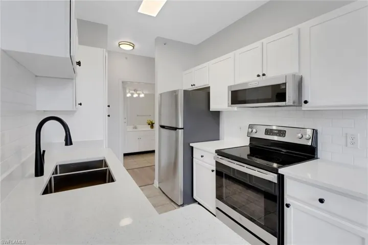 Kitchen with stainless steel appliances, light tile patterned flooring, sink, tasteful backsplash, and white cabinets