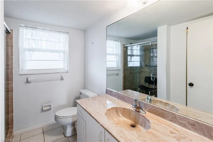 Bathroom featuring a shower with door, vanity, tile patterned floors, and toilet