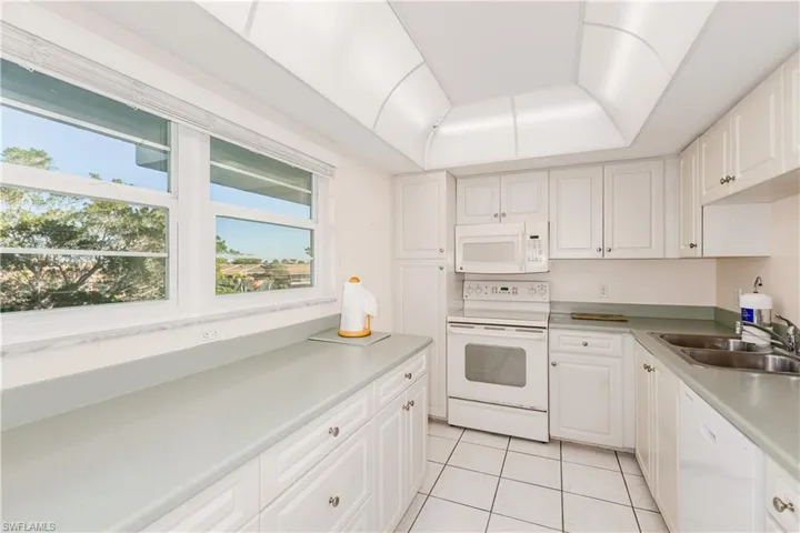 Kitchen featuring light tile patterned flooring, white appliances, sink, and white cabinets