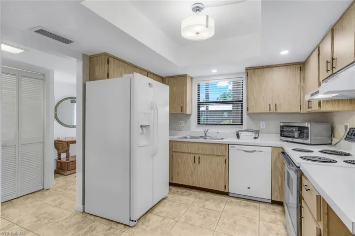 Kitchen with a tray ceiling, white appliances, light tile patterned floors, and sink