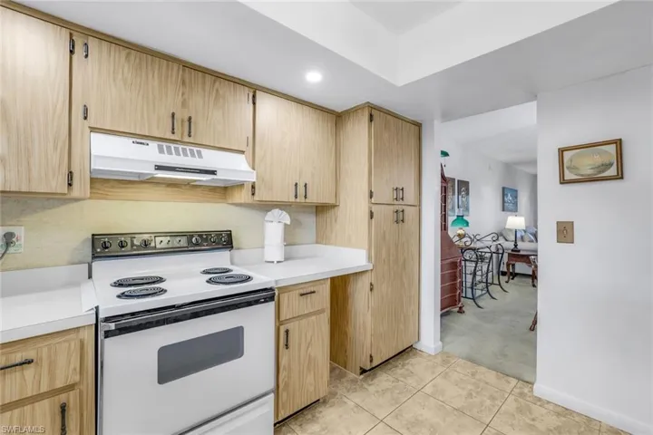Kitchen with white range with electric stovetop, light carpet, decorative backsplash, and light brown cabinetry