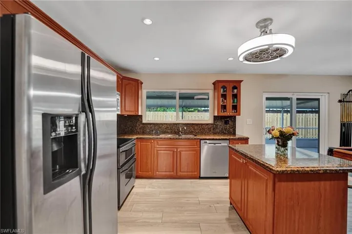 Kitchen featuring appliances with stainless steel finishes, a sink, backsplash, dark stone countertops, and a kitchen island