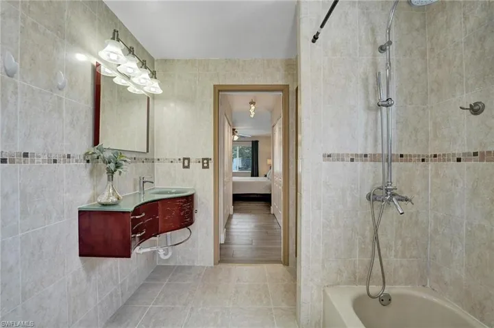 Ensuite bathroom featuring vanity, tile patterned flooring, shower / washtub combination, tile walls, and ceiling fan