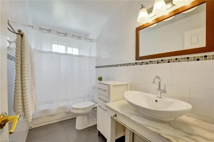 Full bathroom with tile walls, shower / bath combo with shower curtain, toilet, tile patterned floors, and vanity
