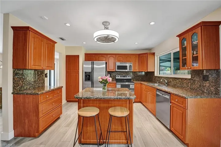 Kitchen featuring appliances with stainless steel finishes, a sink, glass insert cabinets, decorative backsplash, and dark stone countertops