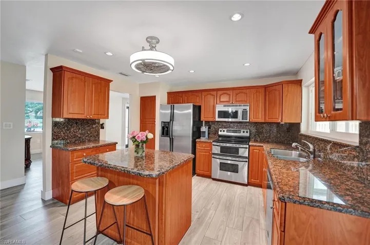 Kitchen with appliances with stainless steel finishes, a sink, glass insert cabinets, a kitchen island, and decorative backsplash