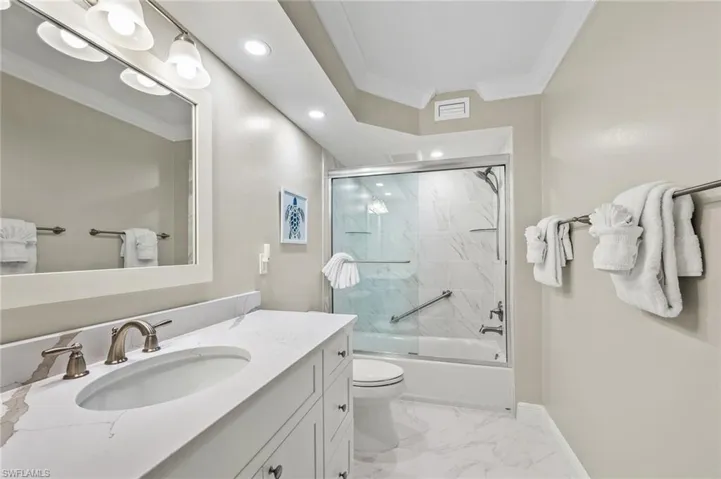 Bathroom with vanity, recessed lighting, ornamental molding, light marble finish flooring, and shower / bath combination with glass door