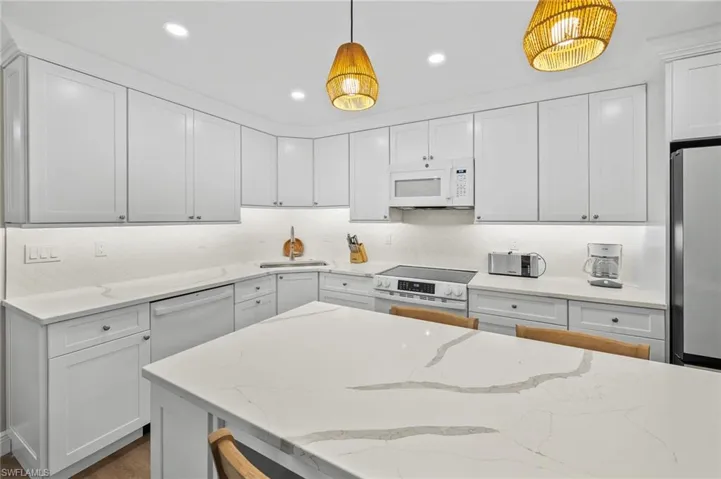 Kitchen featuring stainless steel appliances, light stone counters, white cabinets, and dark wood-style floors