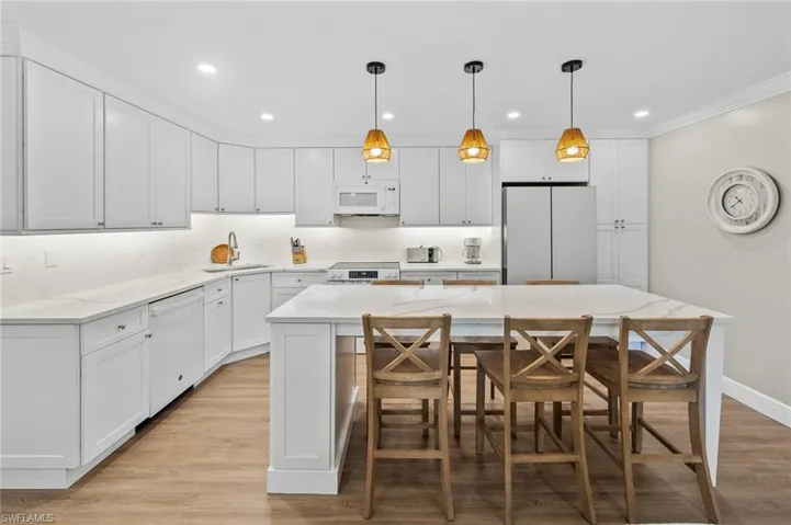 Kitchen featuring light wood-type flooring, white cabinets, white appliances, a breakfast bar, and a center island