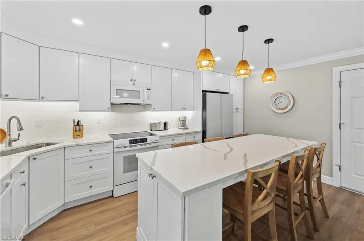 Kitchen featuring white appliances, white cabinetry, light wood finished floors, light stone countertops, and ornamental molding