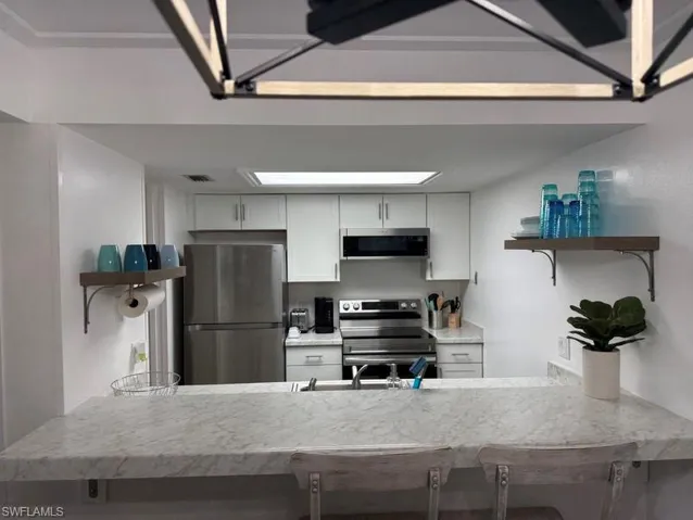 Kitchen with open shelves, white cabinetry, stainless steel appliances, and a peninsula