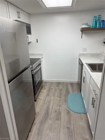 Kitchen with appliances with stainless steel finishes, white cabinets, light countertops, light wood-type flooring, and open shelves