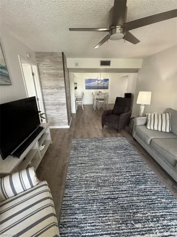 Living area with dark wood-type flooring, a ceiling fan, and a textured ceiling