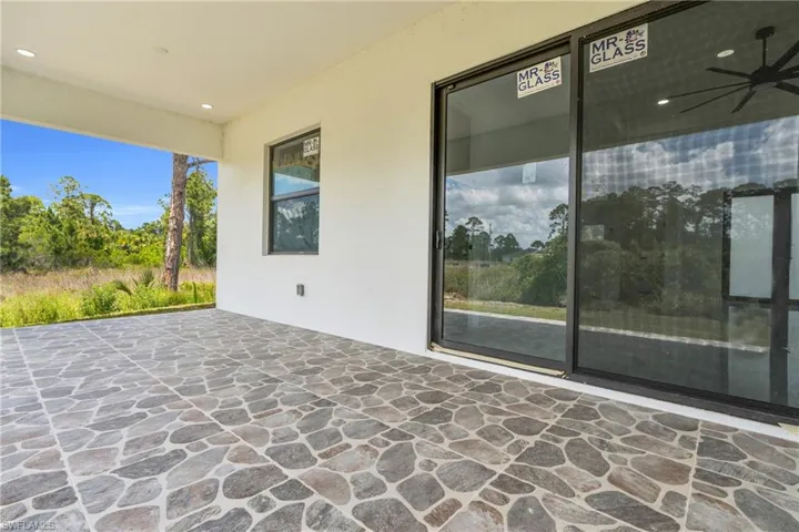 Covered patio featuring irregular-patterned stone-look tile flooring, white stucco walls, recessed lighting, and a black ceiling fan