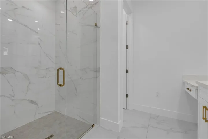 Glass-enclosed shower with large format tile walls and flooring, featuring brass hardware