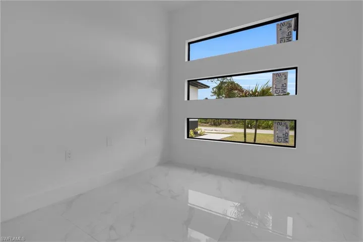 Interior space featuring three horizontal transom windows, white walls, white baseboards, and large format white tile flooring with subtle veining