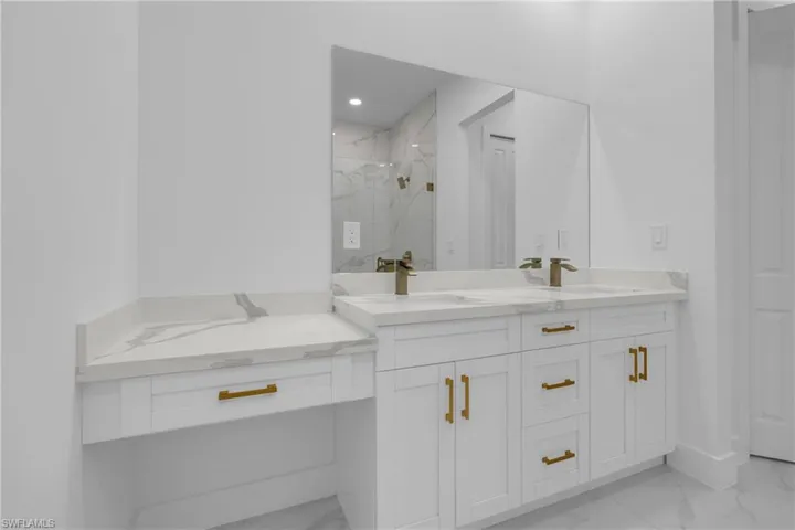 Dual vanity with integrated sinks, quartz countertops, bronze-finish faucets, white shaker cabinetry, and a dedicated vanity seating area