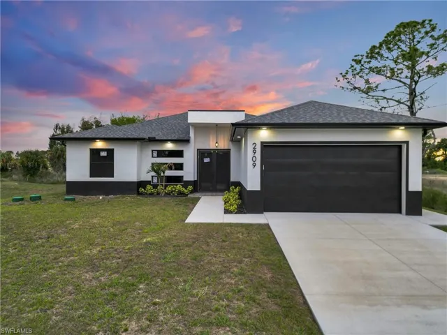 Contemporary single-story residence featuring a two-tone exterior, a dark shingle roof, an attached two-car garage with a dark door, a concrete driveway, and a concrete walkway