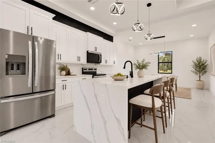 Gourmet kitchen featuring a waterfall island, stainless steel appliances, white cabinetry with black hardware, and contemporary pendant lighting