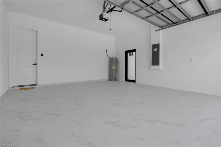 Spacious garage featuring large format tile flooring, white walls, and a finished ceiling with exposed support beams
