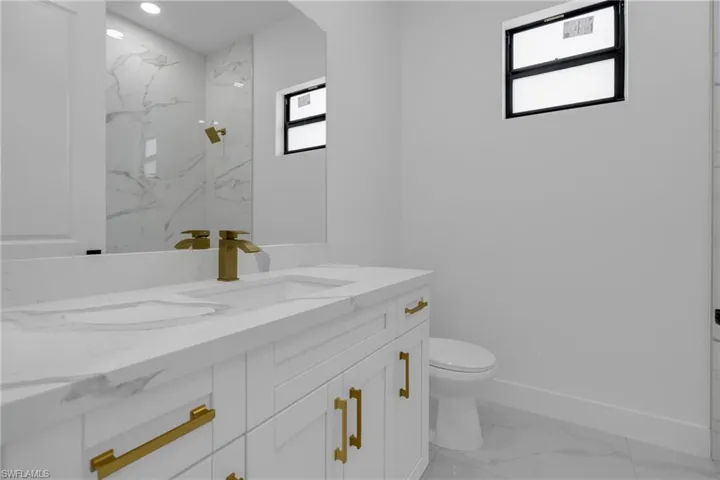 Modern bathroom featuring a white vanity with gold-tone hardware, an integrated sink with a waterfall-style gold-tone faucet, and a large mirror