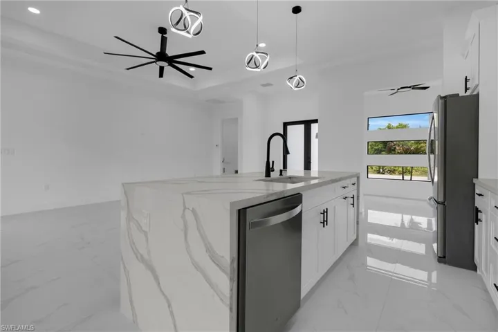 Kitchen island with waterfall-edge countertop, integrated sink with matte black faucet, and stainless steel dishwasher