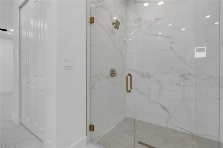 Glass-enclosed shower featuring white marble-look wall tiling, a light gray hex tile shower pan, and gold-tone fixtures