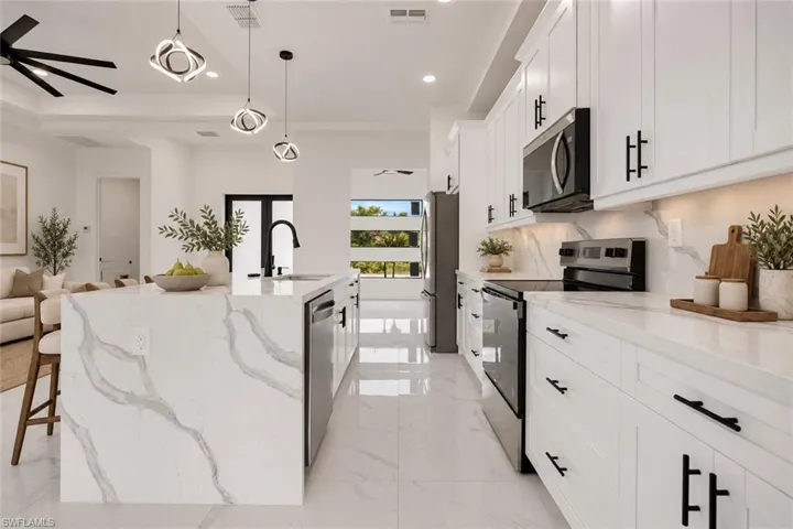 Spacious kitchen featuring an extended waterfall island, white shaker cabinetry with black hardware, stainless steel appliances, and polished tile flooring